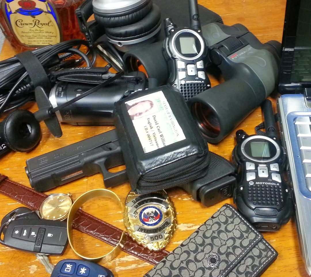 David Carl Williams’s camera, binoculars, radios, badge, ID wallet, handgun, and personal belongings arranged on a wooden desk.